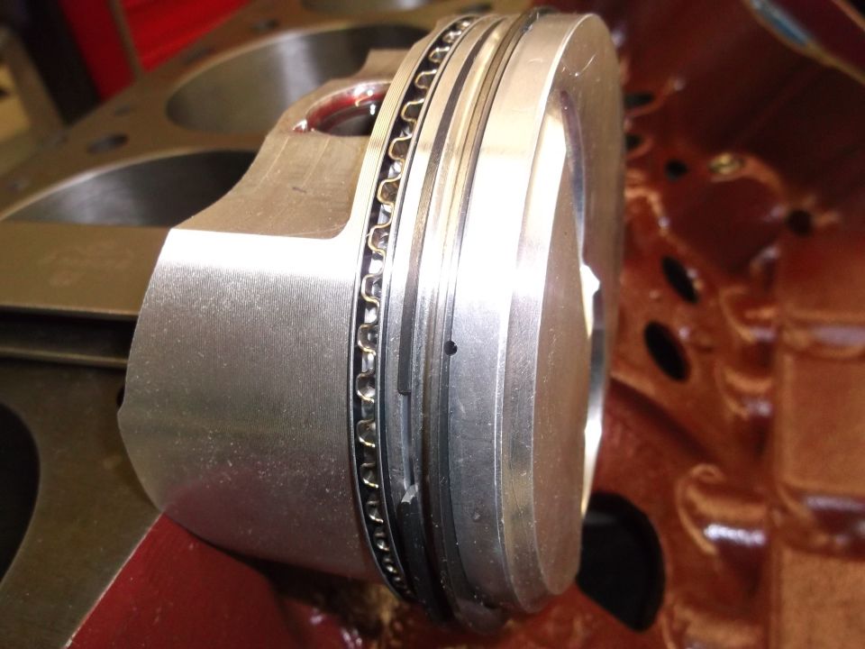 Engine piston with oil rings installed, next to cylinder block