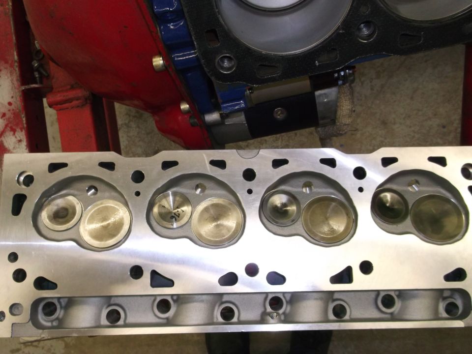 Close-up of an engine cylinder head with valves visible. Part of a red engine block is in the background