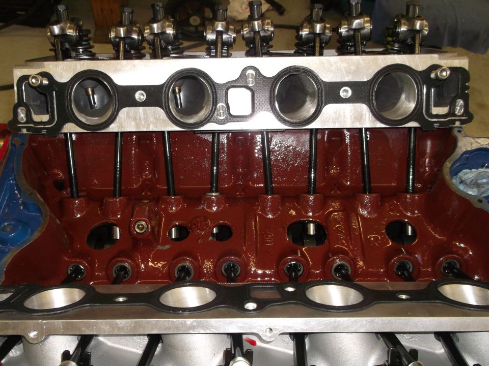 Engine block with cylinder head, pushrods, and gasket installed. Supermotors.net logo visible