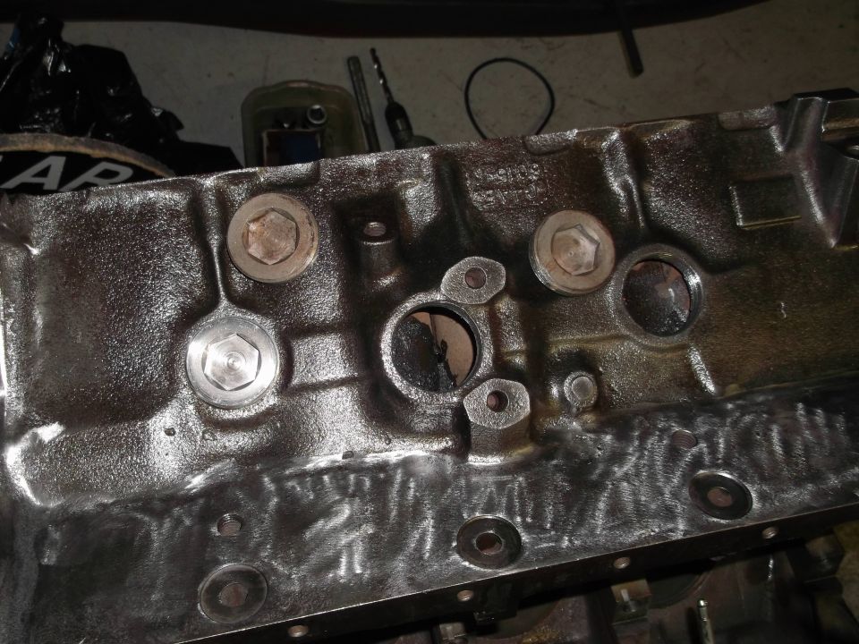 Close-up of a cast iron engine block with several bolt holes and plugs visible