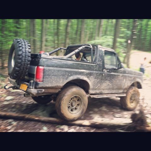 1995 Ford Bronco - A Ford Bronco navigates a muddy trail through a dense forest.