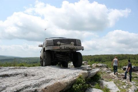 1995 Ford Bronco - A lifted Ford Bronco navigates a rocky trail with two people observing.