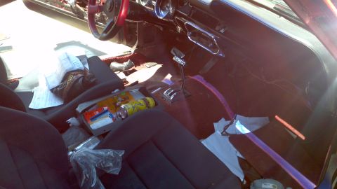 1987 Ford Bronco - The interior of a car shows a cluttered dashboard and seats with various items strewn about.