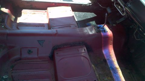 1987 Ford Bronco - The interior of a red vehicle shows the floor and transmission tunnel, with some rust and wear visible.