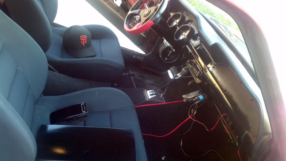 Interior view of a vehicle with blue seats, a black baseball cap, and exposed wiring