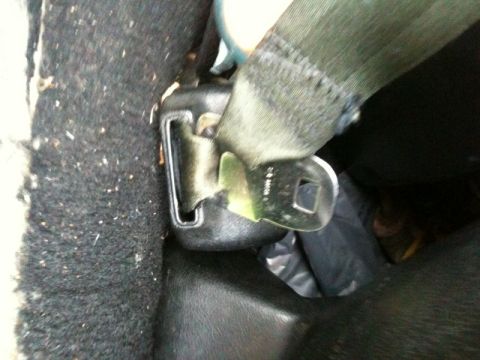 1975 Chevrolet Chevelle - Close-up of a car's seatbelt buckle mechanism, showing the metal clasp and green fabric strap.