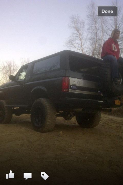 1995 Ford Bronco - A black Ford Bronco is viewed from the rear, lifted with large tires, while a woman sits on the spare tire carrier.