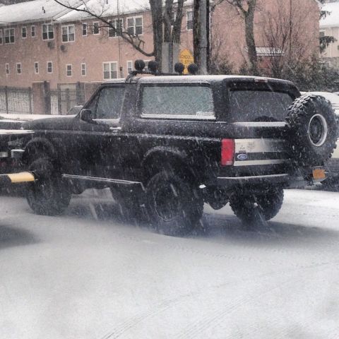 1995 Ford Bronco - A black 1995 Ford Bronco navigates a snowy road, its spare tire mounted externally.