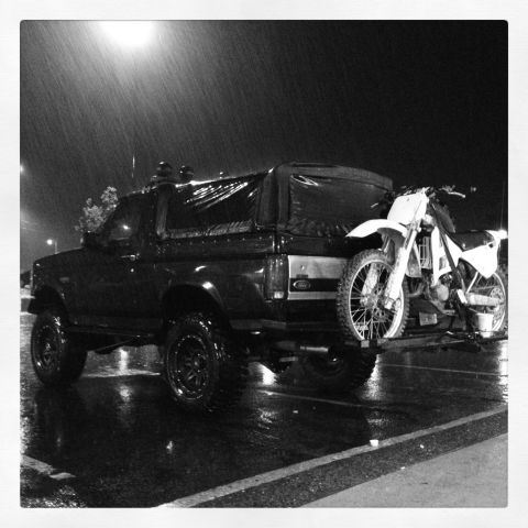 1995 Ford Bronco - A black Ford Bronco is parked on a wet street at night with a dirt bike attached to its rear.