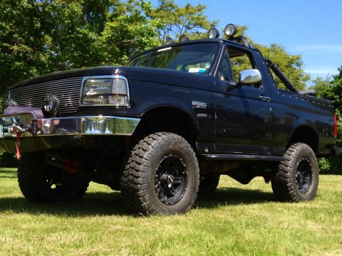 1995 Ford Bronco - Modified 1995 Ford Bronco with off-road tires and roof-mounted lights sits on a grassy lawn.