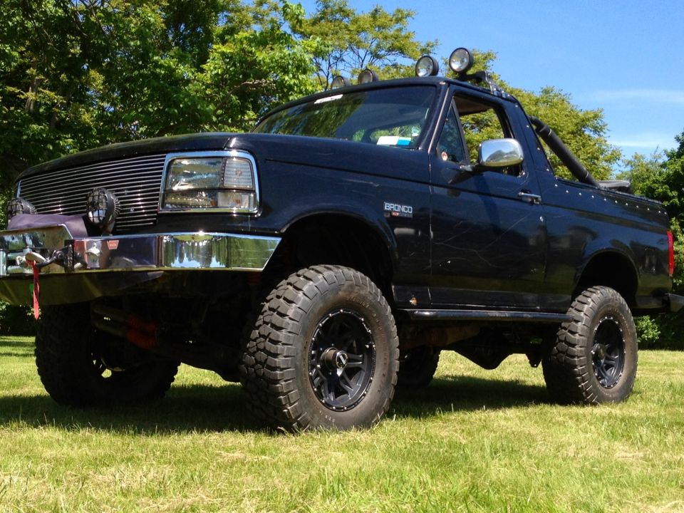1995 Ford Bronco with aftermarket grille, lights, and off-road tires parked on grass