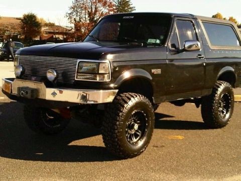 1995 Ford Bronco - This lifted black Ford Bronco features an aftermarket grille and bumper, with large off-road tires.