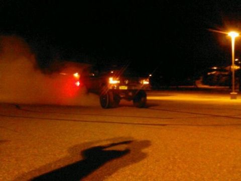 1995 Ford Bronco - A vehicle performs a burnout at night, illuminated by streetlights and its own taillights.