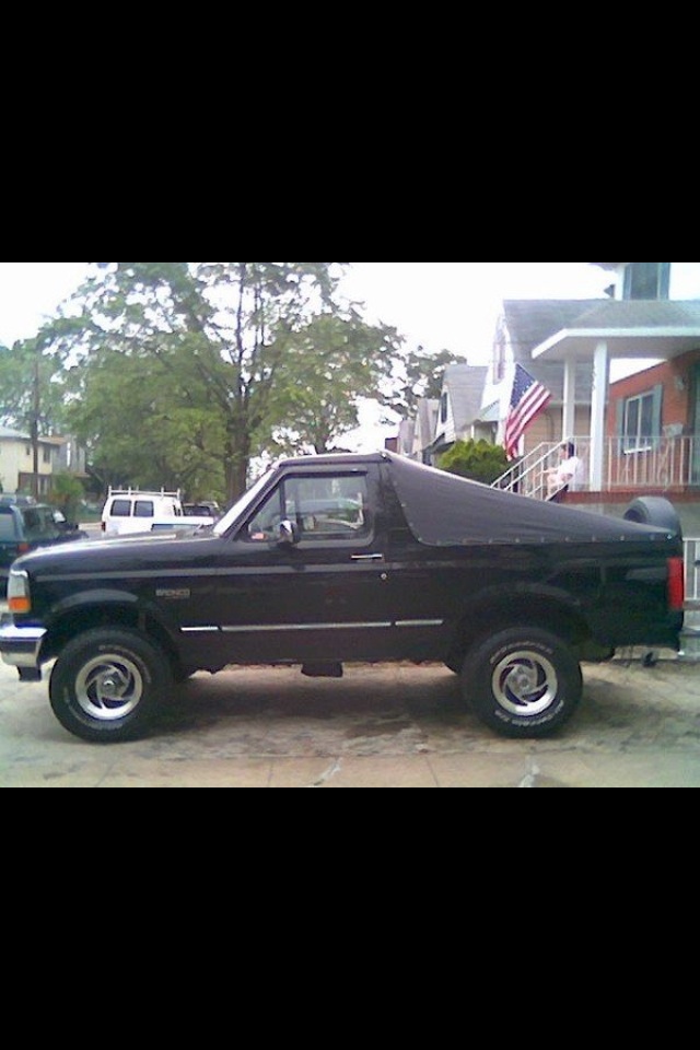 Black Ford Bronco parked on a street, side view. Has a soft top cover over the rear