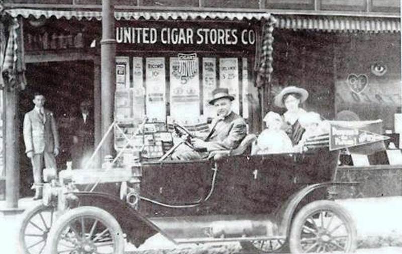 1912 Ford Model T with passengers in front of United Cigar Stores Co