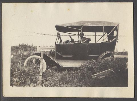 1912 Ford Model T - A vintage touring car with its top up is seen parked beside a barbed wire fence, with occupants inside.
