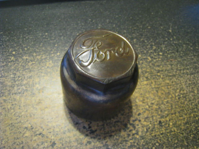 Tarnished brass Ford script hub cap with hex flats resting on a dark workbench