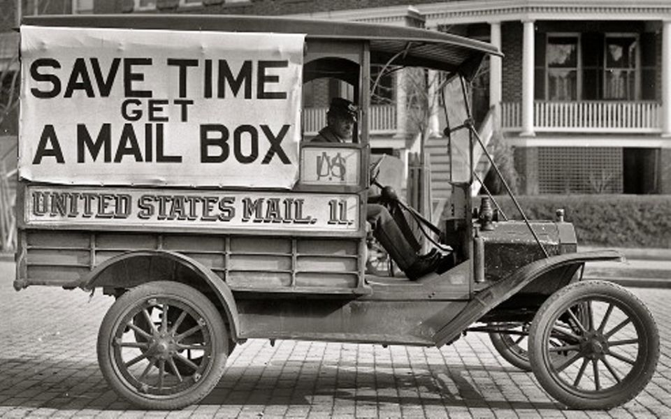 Antique US Mail Model T delivery truck with SAVE TIME GET A MAIL BOX banner on a brick street