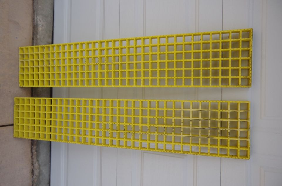 Two yellow grates with square openings, one above the other, against a white paneled background