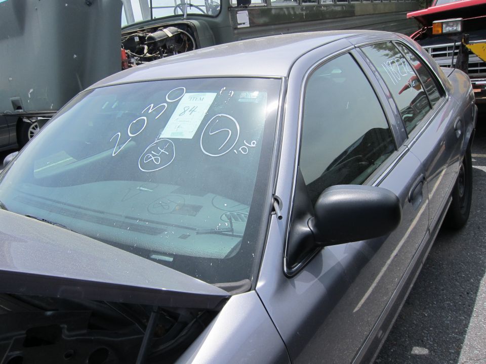 Gray sedan with writing on windshield, parked near a truck and a red vehicle