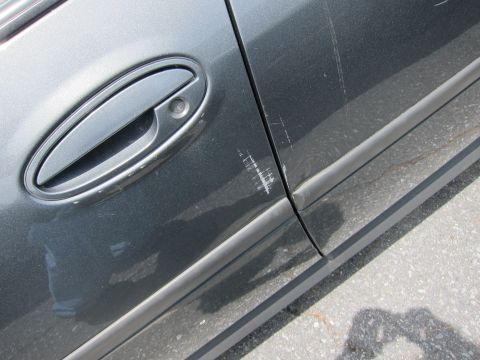 1991 Ford LTD Crown Victoria - The side of a car shows significant scratches on the paintwork near the door handle and trim.