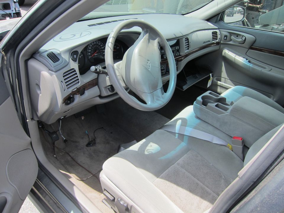 Car interior with light grey seats, dashboard, and steering wheel. Wires are visible on the floor