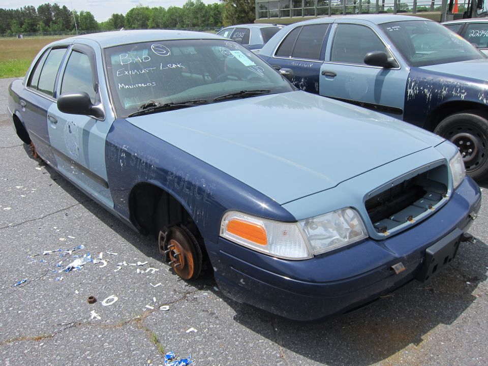 Two-tone blue police car with missing wheels and front grille, showing "POLICE" text on fender
