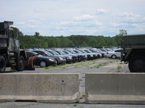 1991 Ford LTD Crown Victoria - A large parking lot filled with numerous cars and two military trucks is visible under a partly cloudy sky.