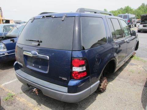 1991 Ford LTD Crown Victoria - A blue Ford Explorer SUV is seen from the rear, missing all four wheels, in a junkyard setting.
