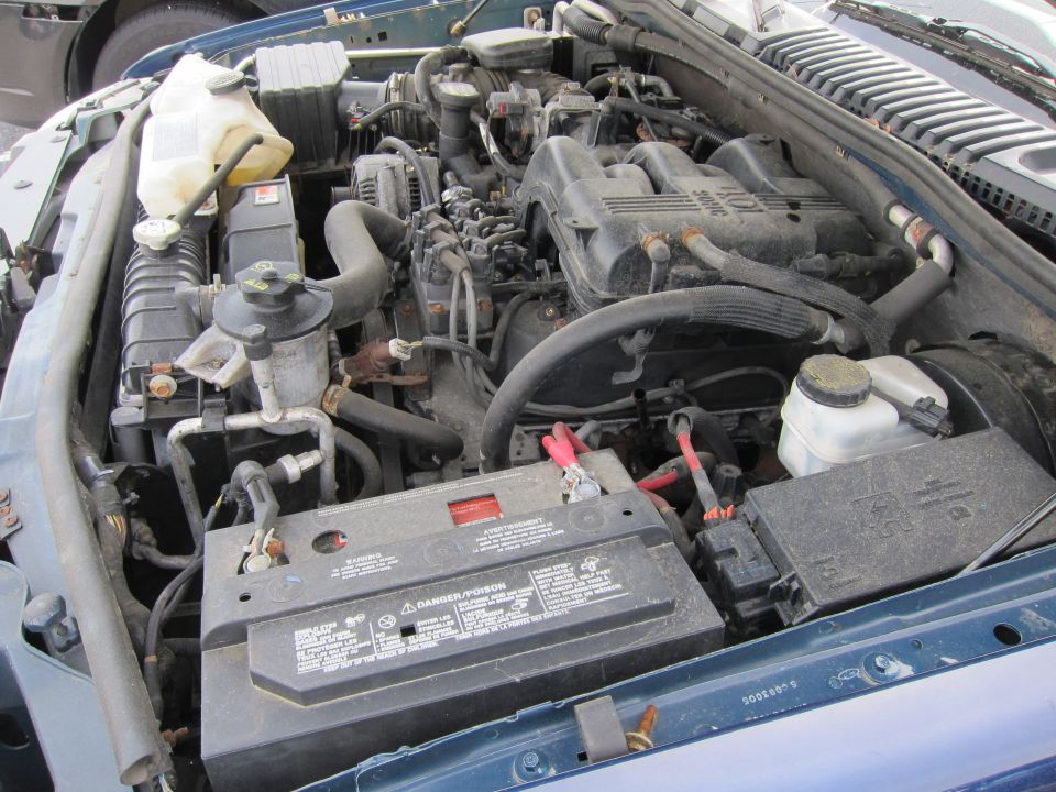 Engine bay of a teal vehicle with a V8 engine, battery, and radiator visible