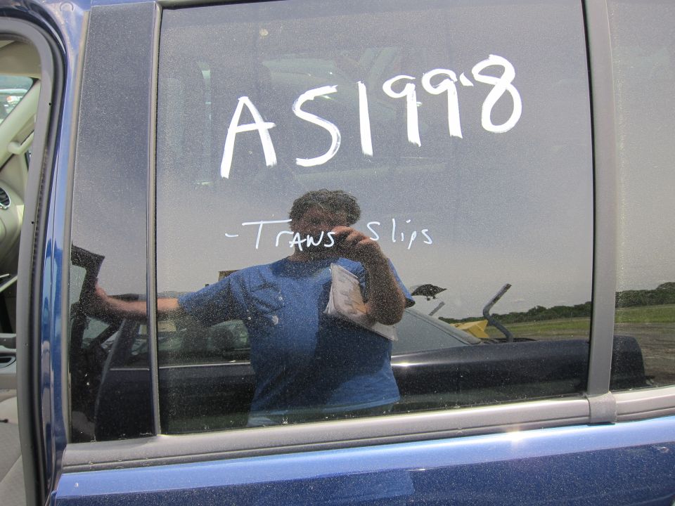 Reflection of person holding camera in blue car window, with 'AS1998' and '-Trans slips' written on glass
