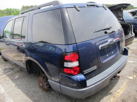 1991 Ford LTD Crown Victoria - A blue Ford Explorer SUV is seen from the rear in a junkyard, missing its wheels and with the hood ajar.
