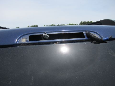 1991 Ford LTD Crown Victoria - Close-up of the rear window trim on a blue vehicle, showing exposed wiring and a connector where a light or emblem may have been.