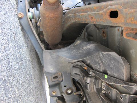 1991 Ford LTD Crown Victoria - The undercarriage of a vehicle displays significant rust on its frame components and a protective plastic shield.