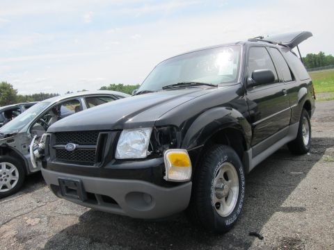 1991 Ford LTD Crown Victoria - A black Ford Explorer SUV sits in a junkyard with visible damage to its front end and its rear hatch ajar.