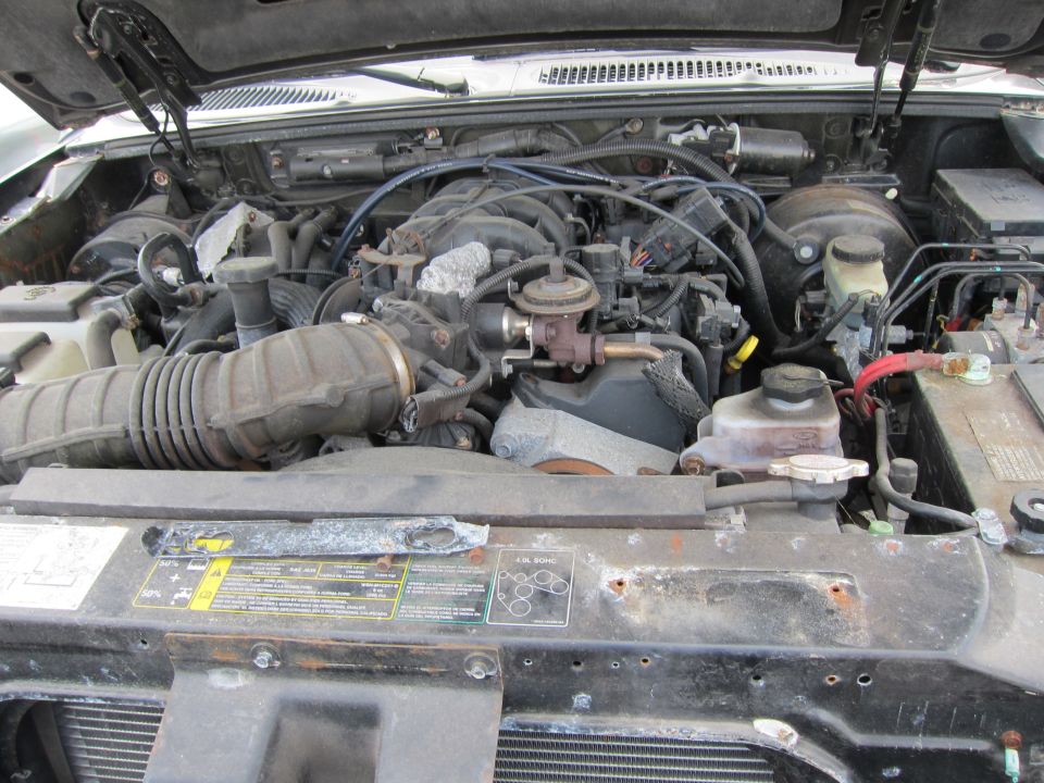Engine bay with V6 engine components, air intake, battery, and various hoses visible. Some labels are present on the radiator support