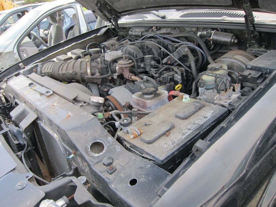 Engine bay with battery, radiator, and engine components visible. Another vehicle is partially seen to the left