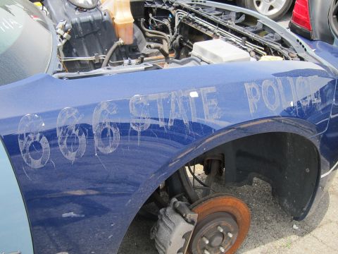 1991 Ford LTD Crown Victoria - Fender of a damaged blue police car with visible lettering and rusty brake components.