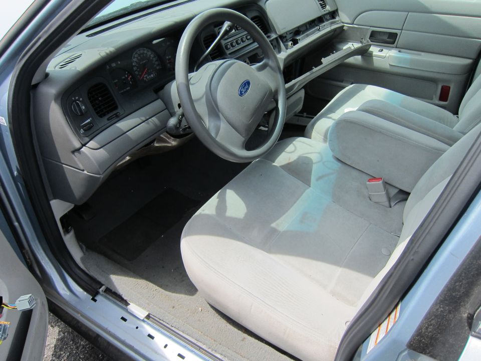 Interior view of a light blue Ford Crown Victoria with light grey cloth seats and a grey dashboard. The glove box is open