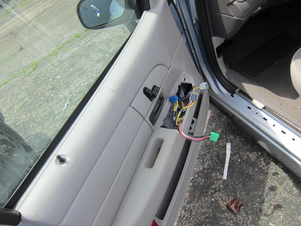Car door panel removed, showing wiring harness and window controls. Exterior view through the open door