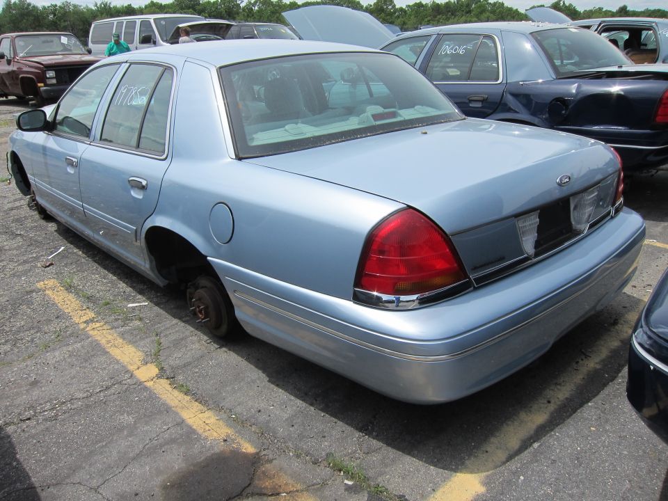 Light blue sedan with missing wheels, rear view. The body style is consistent with a 2003 Ford Crown Victoria