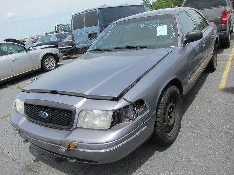 1991 Ford LTD Crown Victoria - A gray Ford Crown Victoria sits in a lot with its hood up and one headlight missing. A blue van and other cars are visible.