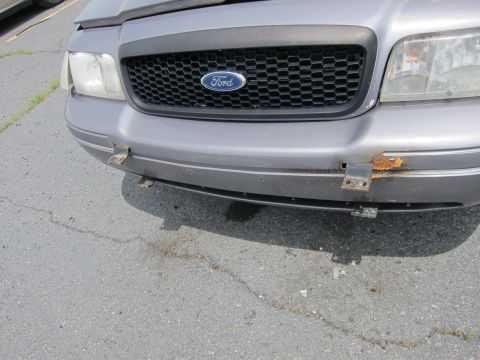 1991 Ford LTD Crown Victoria - Front view of a grey Ford Crown Victoria, showing the grille, headlights, and bumper with visible rust and mounting brackets.