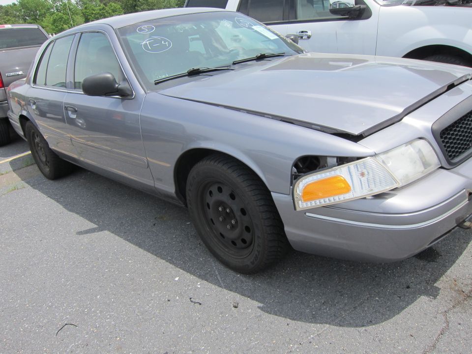Gray Ford Crown Victoria with missing headlight and dented front end. Another vehicle is parked behind it