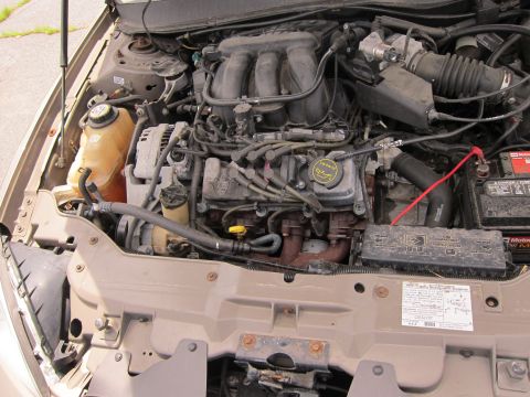 1991 Ford LTD Crown Victoria - The engine bay of a car, a V6 engine, coolant reservoir, and battery, with some visible text on a label.