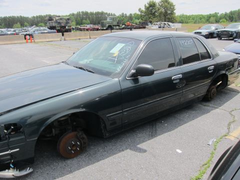 1991 Ford LTD Crown Victoria - Sedan missing wheels in a salvage yard. White markings on the windshield and a number on the door are visible.