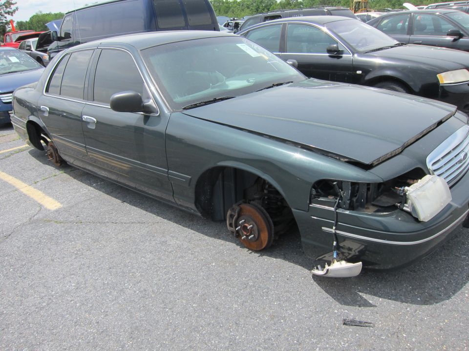 Green Ford Crown Victoria with missing wheels and damaged front end parked in a lot