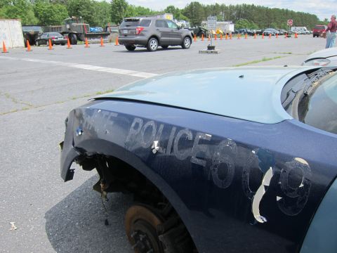 1991 Ford LTD Crown Victoria - A damaged police car fender with "STATE POLICE 609" visible, parked in an outdoor lot with other vehicles and equipment.