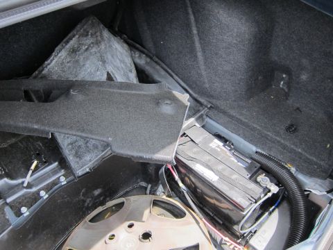1991 Ford LTD Crown Victoria - View of a car's trunk interior, revealing the battery, spare tire well, and a detached trim panel.