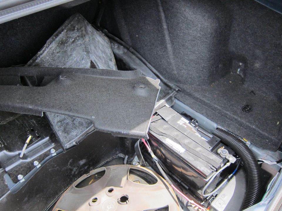 Trunk interior showing battery, spare tire well, and removed panel
